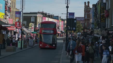 Red-Double-Decker-Bus-Driving-On-High-Street-In-Camden-Town,-London-With-Crowd-Of-Pedestrians-Walking-On-Sidewalks-At-Daytime