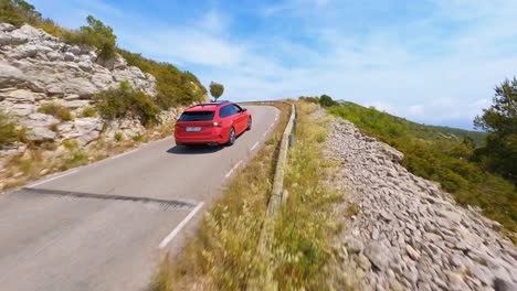 FPV-aerial-following-a-red-car-driving-along-a-scenic-highway-in-the-Spanish-countryside