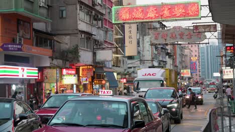 Fahrzeuge-Warten-An-Einer-Ampel.-Über-Ihnen-Hängt-Eine-Geschäftsleuchtreklame-An-Der-Fassade-Eines-Wohngebäudes-In-Hongkong