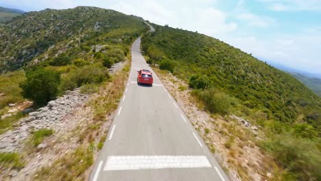 FPV-aerial-tracking-a-red-station-wagon-driving-through-a-scenic-mountain-landscape