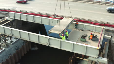 Construction-workers-securing-lowering-of-road-bridge-slab-from-crane