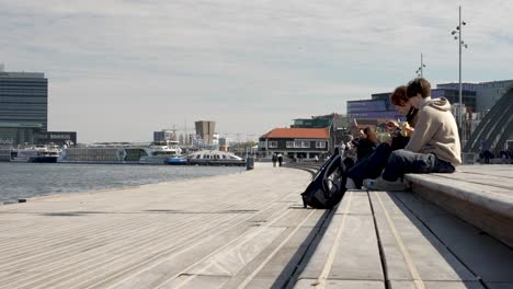 Couple-Sitting-On-Boardwalk-Having-Lunch-Beside-The-IJ-River-In-Amsterdam