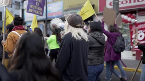 Eine-Blonde-Frau-Spricht-Durch-Ein-Megaphon,-Während-Sie-Neben-Frauen-Marschiert,-Die-Während-Des-Protestes-Zum-Internationalen-Frauentag-In-Quito,-Ecuador,-Schilder-Und-Fahnen-Hochhalten