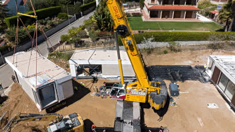 Crane-placing-modular-house-block-into-place,-aerial-hyper-lapse-view