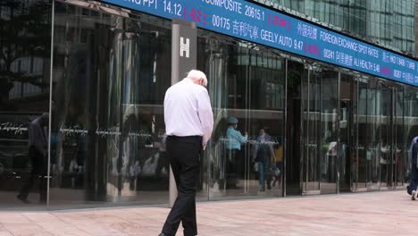 People-walk-past-an-electronic-ticker-board-and-screen-displaying-stock-market-figures-outside-the-Exchange-Square-complex,-which-houses-the-Hong-Kong-Stock-Exchange