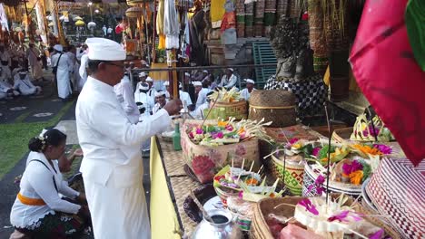 Priest-of-Balinese-Hinduism-Performs-Cleansing-Ceremony-with-Colorful-Offerings-in-Worshiping-Temple-at-Bali-Indonesia,-People-Praying-Outdoors,-Daylight