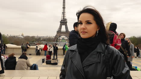 Beautiful-Brunette-Standing-in-Front-of-the-Eiffel-Tower,-Looking-into-the-Camera,-Slow-Motion-Cinematic-Close-Up,-People-in-the-Background