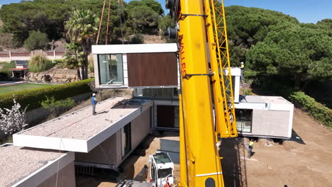 Construction-workers-with-heavy-crane-building-luxury-modular-home,-aerial-drone-view