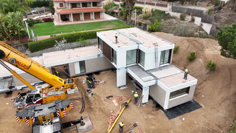 Construction-site-of-modular-home-with-heavy-crane,-aerial-orbit-view