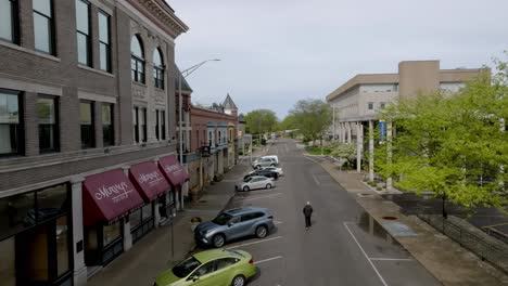 Man-walking-down-a-street-in-downtown-Muncie,-Indiana-with-drone-video-following