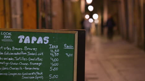 Local-Bar-Restaurant-Tapas-Menu-on-Blackboard-on-Streets-of-Barcelona,-Spain-at-Night,-Handheld