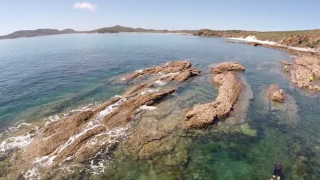 Drone-over-snorkeller-exploring-rocks-near-the-great-barrier-reef,-Australia