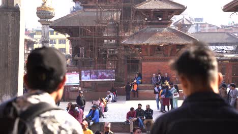 Disparo-Desde-Detrás-De-Dos-Amigos-Varones-Nepaleses-Hablando,-El-Foco-Principal-En-El-Templo-En-La-Parte-Trasera-Katmandú-Nepal