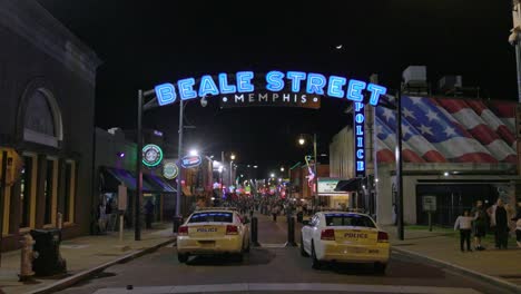 Beale-Street-sign-in-Memphis,-Tennessee-at-night-with-two-police-cars-and-gimbal-video-walking-forward