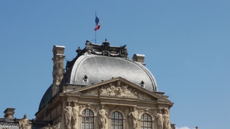 French-flag-waving-in-the-Western-facade-of-the-Pavillon-Sully,-courtyard-of-the-Louvre-Palace-in-Paris,-France