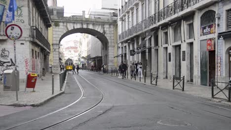 A-yellow-tram-arrives-at-Cais-Sodre,-in-the-center-of-Lisbon,-Portugal,-as-people-walk-by