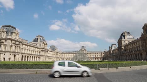 Traffic-passing-through-with-the-courtyard-of-the-Louvre-Pyramid-and-Palace-in-the-background-in-Paris,-France