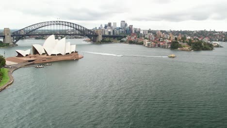 Sydney,-New-South-Wales,-Australia---24-December-2021:-Ferry-and-boat-in-Sydney-Harbour-and-moving-in-close-to-the-Sydney-Opera-House-with-the-Sydney-Harbour-Bridge-in-the-background
