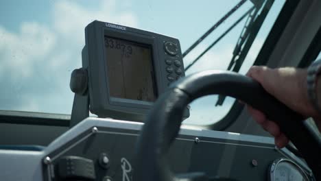 Close-up-of-depth-finder-or-fish-finder-with-GPS-on-fishing-boat-with-hand-on-steering-wheel-steering-boat