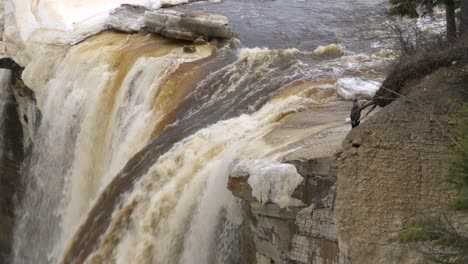 Man-stands-at-edge-of-Alexandra-Falls-Northwest-Territories-looking-down-during-spring-breakup