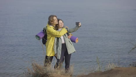 Traveler-couple-smiling-and-posing-taking-selfie-using-smartphone-standing-on-top-of-the-cliff