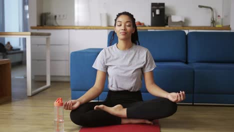 African-american-woman-is-sitting-lotus-pose-on-yoga-mat-floor-closed-eyes