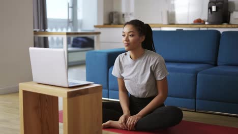 Junge-Frau-Spricht-Per-Videoanruf-Auf-Dem-Laptop,-Während-Sie-Auf-Einer-Yogamatte-Sitzt