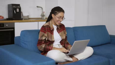 Positive-girl-with-dreadlocks-is-laughing-and-smiling-with-laptop-on-knees