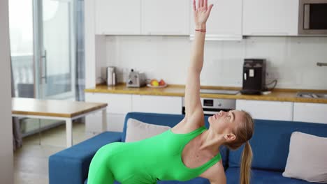 Slender-lady-in-green-tracksuit-performs-standing-asanas-Trikonasana,-The-Triangle-Pose-using-yoga-blocks-for-support