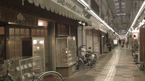 Empty-Tokyo-shopping-market-arcade-with-bikes-parked-outside-store---people-walking-in-the-distance