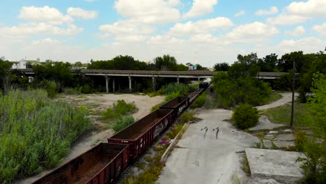 A-drone-shot,-with-upward-and-downward-pedestal-motion,-capturing-horizontal-highways-in-distance-and-a-goods-train-passing-from-under-them-and-trees-sorrounding-the-entire-scene-and-a-bright-blue-sky