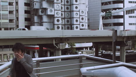 Asian-family-walking-passing-camera-ground-level-panning-up-to-with-to-top-of-Nakagin-Capsule-Tower-in-Tokyo