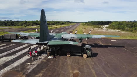 Orbital-aerial-shot-of-soldiers-unloading-a-cargo-plane,-loading-a-military-truck-on-a-runway
