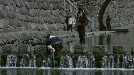 Japanese-policeman-searching-for-something-in-water-with-a-female-watching-over-him