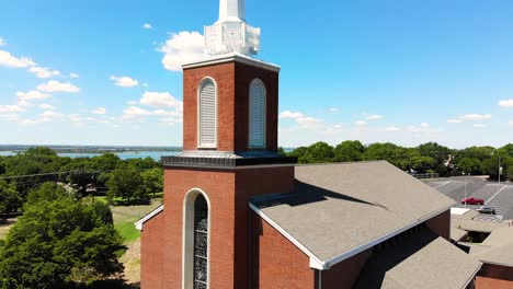 A-drone-shot,-with-upward-pedestal-motion,-over-a-church-with-a-view-of-the-entire-city-covering-trees,lake-and-the-street-with-bright-blue-sky-covered-with-clouds-in-the-background