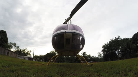Low-angle-shot-of-a-Bell-type-utility-helicopter-waiting-on-the-ground-with-engines-on,-rotating-blades
