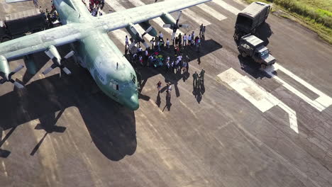 Pull-back-aerial-shot-as-people,-solders-gathering-around-a-military-cargo-ship-on-a-runway