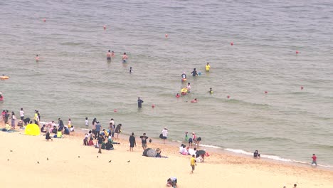 Medium-Close-up-of-people-in-the-water-and-on-the-beach-at-Haeundae-beach,-Busan,-South-Korea