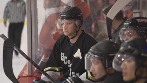 Assistant-captain-in-uniform-sits-on-the-bench-watching-other-hockey-players-play