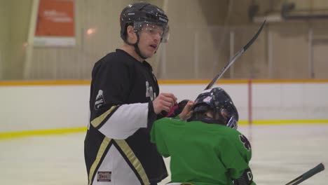 Adult-hockey-player-helps-younger-player-adjust-helmet