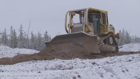 Wide-shot-of-bulldozer-pushing-snow-covered-dirt-on-job-site
