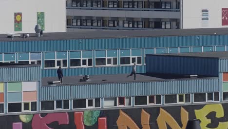 Locked-Off-View-Of-Two-Youths-Running-On-Rooftop-Playing-Tag-On-Building-In-Nuuk,-Greenland