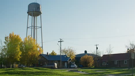Water-tower-next-to-a-park-in-a-small-town-in-autumn-with-beautiful-fall-colors-in-the-evening-sun