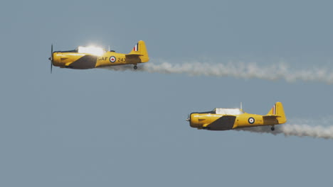 Close-up-of-two-North-American-Harvard-Mark-IV-airplanes-performing-flyby-with-sun-reflecting-off-of-cockpit-at-airshow-in-slow-motion