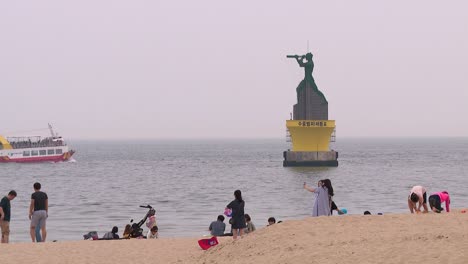 People-on-Haeundae-Beach,-ferry-passing-a-marine-marker-in-the-background