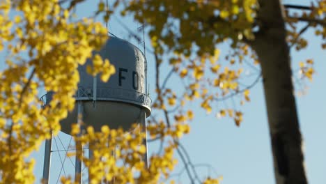 Shot-of-water-tower-through-trees-and-yellow-leaves-in-the-evening-sun