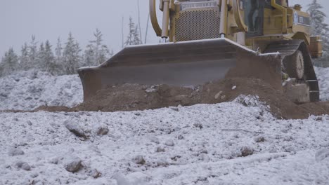 Bulldozer-pushes-snow-covered-dirt-on-barren-landscape