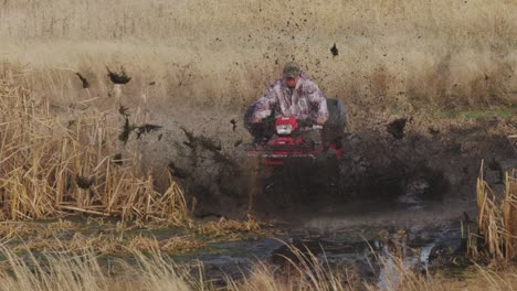 Man-riding-quad-ATV-into-mud-swamp-had-on-with-mud-flying-everywhere