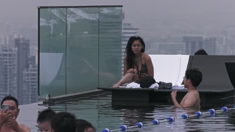 Tourist-couple-pleasantly-enjoying-Infinity-Pool-at-Marina-Bay-Sands-in-Singapore---Long-static-medium-wide-shot