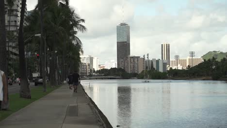 Gente-Caminando-Tranquilamente-En-El-Paseo-Marítimo-Junto-Al-Canal-Ala-Wai-En-Oahu,-Hawaii---Plano-Estático-Amplio